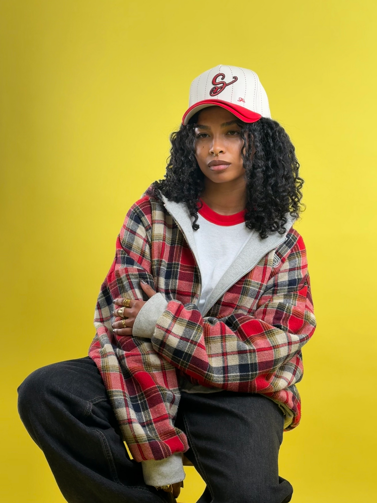 Person wearing a plaid jacket, white shirt, and red cap on a yellow background